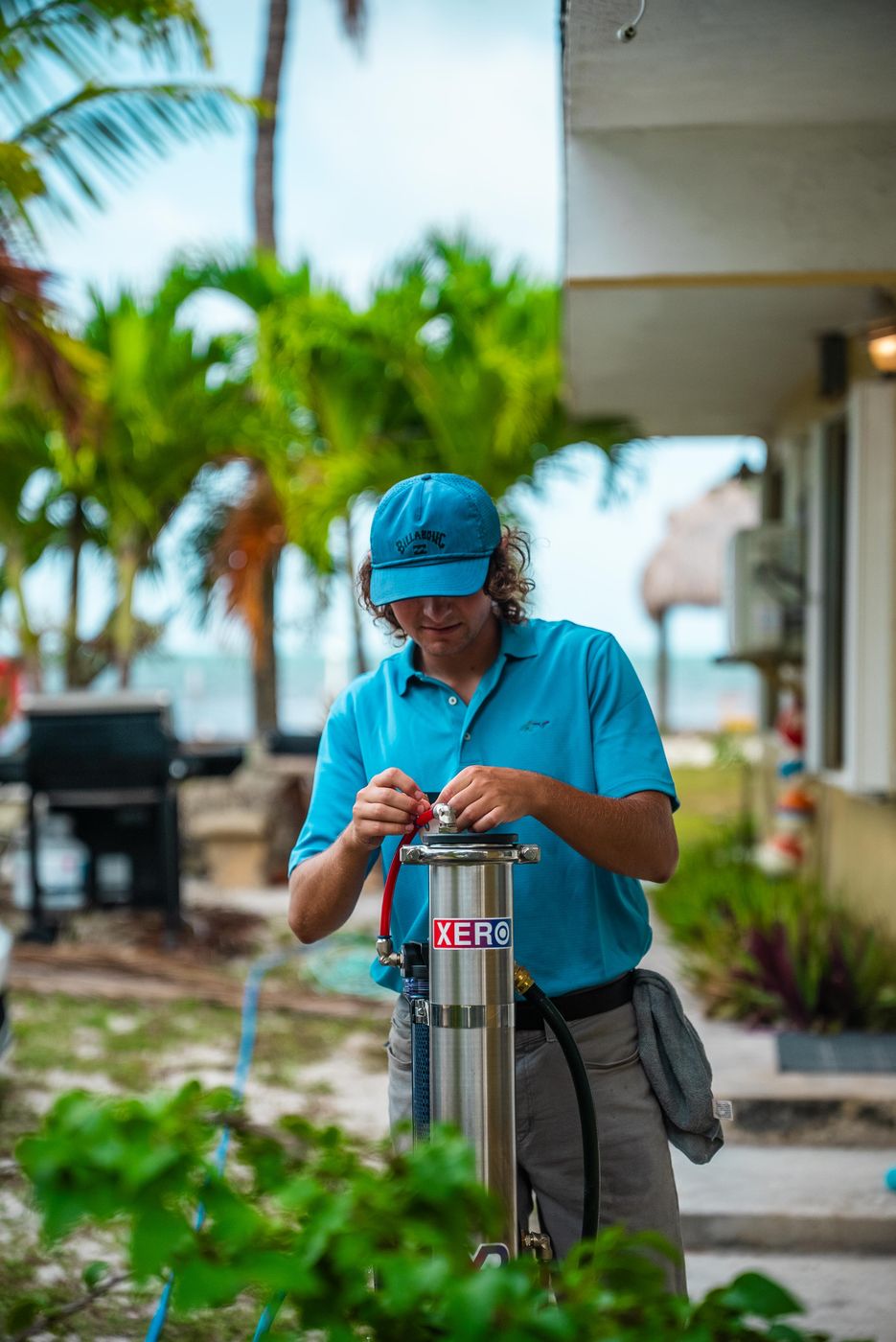 Sea Clear technician connecting hoses to the stainless pure-water filtration tank outside a Florida Keys home, palm trees and water behind