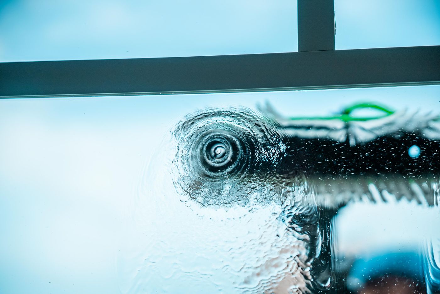 Pure water sheeting across glass mid-rinse, sky showing through the clean pane